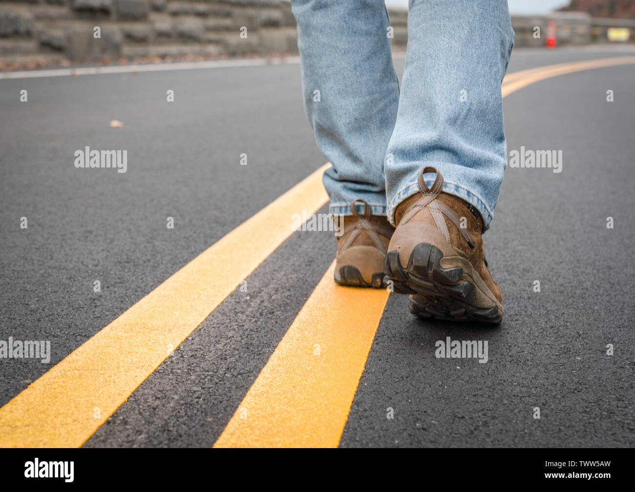 Close up of the legs of a person walking in the middle of the road on the yellow line. Stock Photo