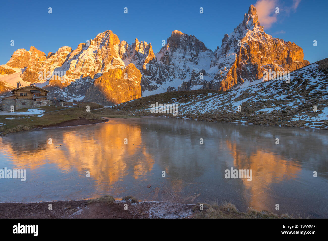Golden mountains reflected on the water of a frozen lake in the Italian Dolomites. Mountain range during golden hour, water reflections of peaks. Stock Photo