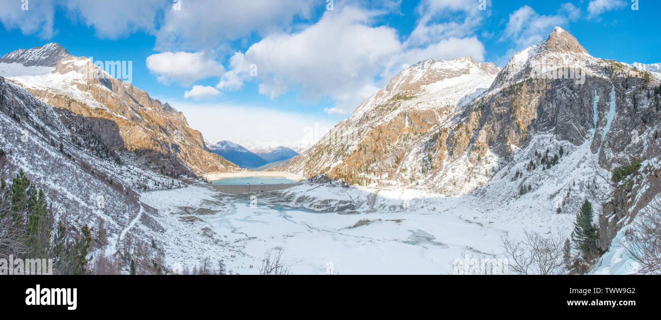 Panoramic view of Lake Avio in the Adamello Brenta national park, Italy. Snowcapped mountains and valley with frozen artificial lake and dam. Stock Photo