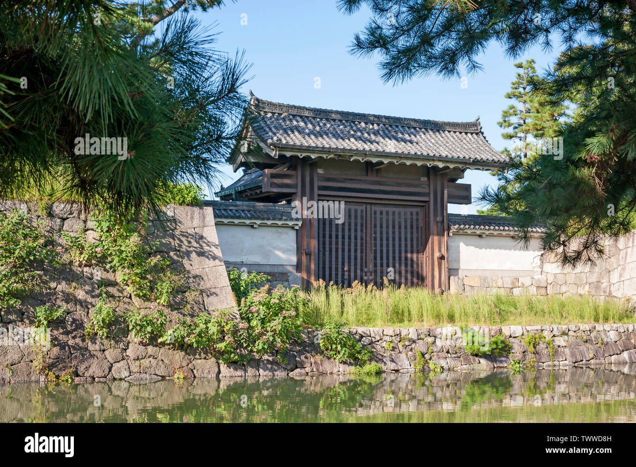 Wooden west gate (Nishi-mon) opening above stone wall onto moat from the grounds of Nijo castle complex, Kyoto, Japan. Stock Photo