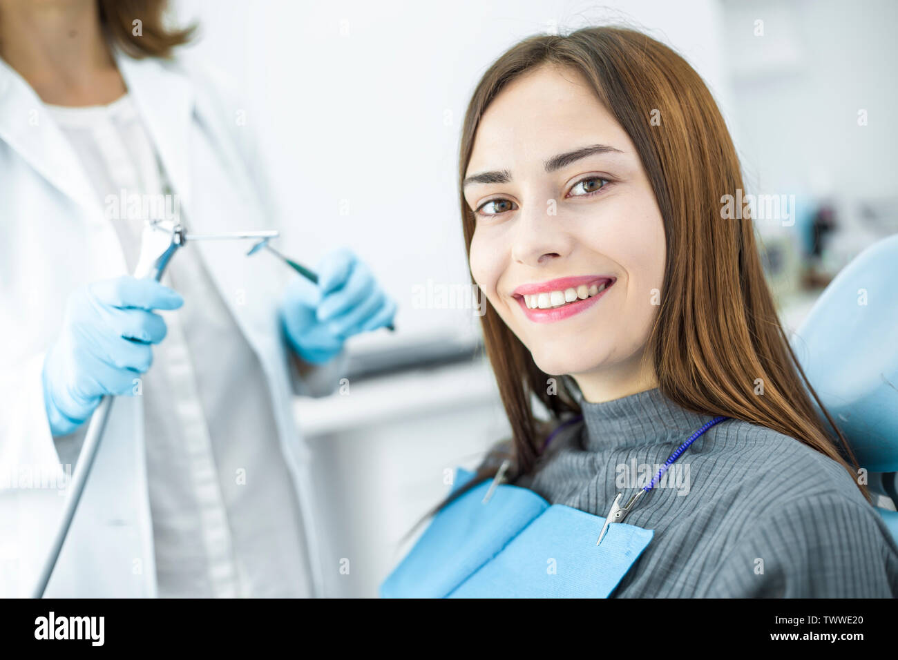 A woman is smiling with white and healthy teeth while sitting in a dental chair. Doctor dentist and happy patient in the office of a medical clinic. Stock Photo