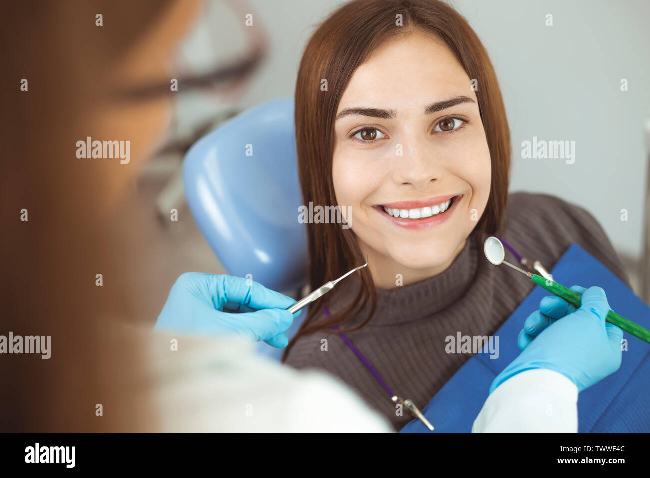 A woman is smiling with white and healthy teeth while sitting in a dental chair. Doctor dentist and happy patient in the office of a medical clinic. Stock Photo