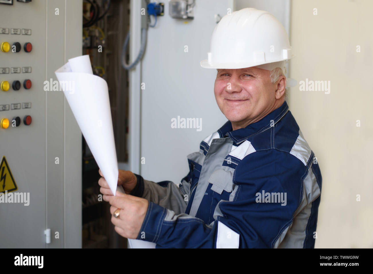 foreman electrician examines the working draft next to the dashboard. Energy and electrical safety Stock Photo