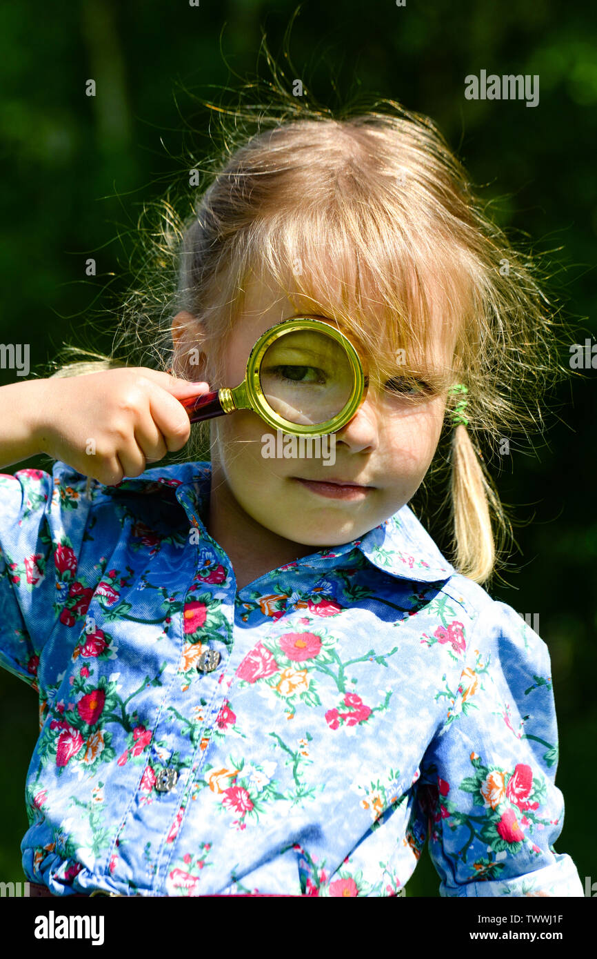 The child looks through a magnifier. Beautiful little girl looking through a magnifying glass. Stock Photo