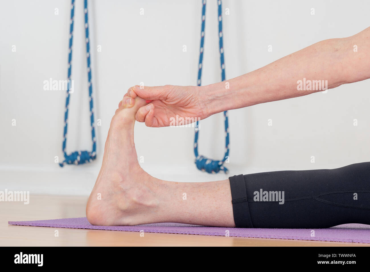a detail of a 70 year old yoga instructor in her studio does  Wide-Angle Seated Forward Bend, aka Upavistha Konasana Stock Photo