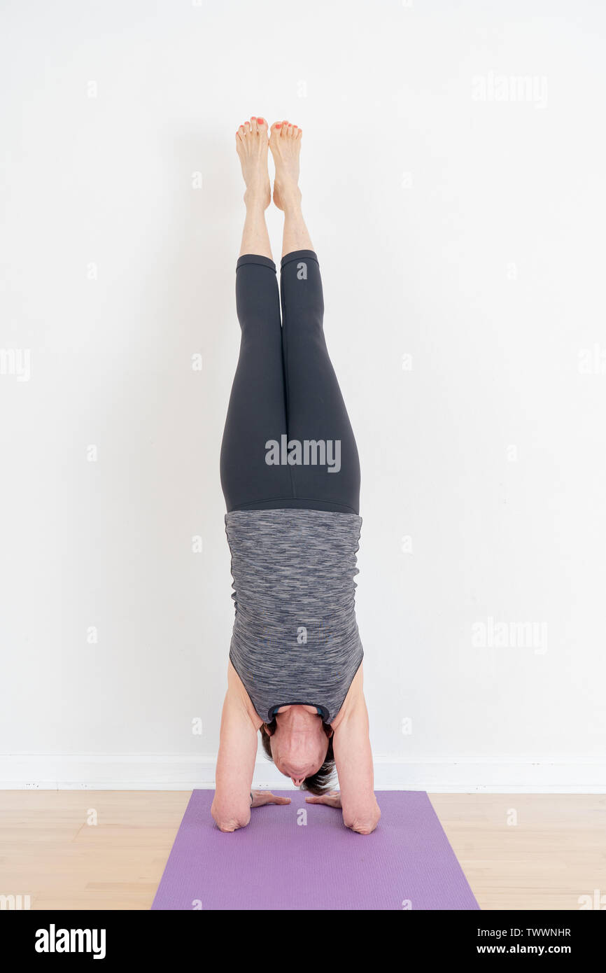 Salamba Sarvangasana, Shoulderstand done with a wall for support by a 70  year old yoga instructor. Viewed from the side Stock Photo - Alamy