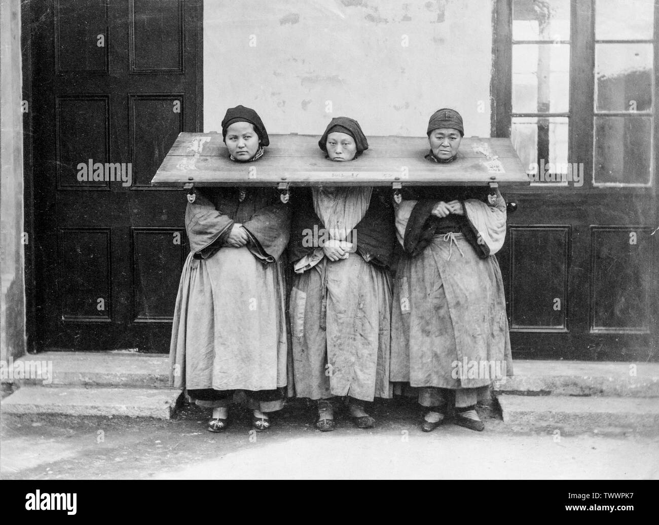 A late 19th century, or early 20th century vintage black and white photograph showing three Chinese women locked in a Cangue, a device used for public humiliation or sometimes torture in may parts of Eastern Asia. Stock Photo