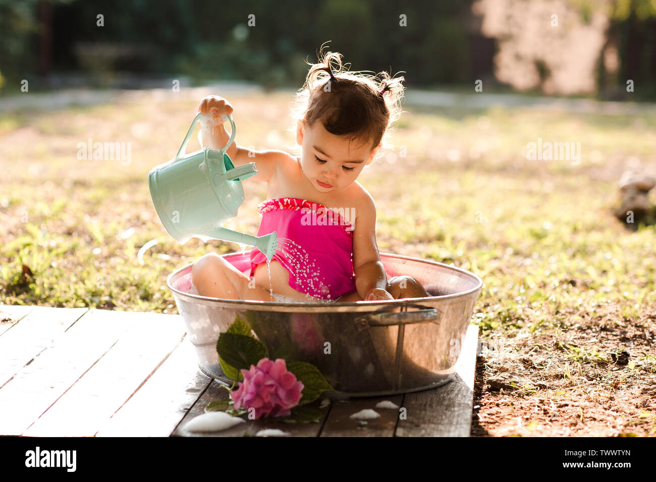 Cute baby having bath outdoors playing with watering can. Childhood