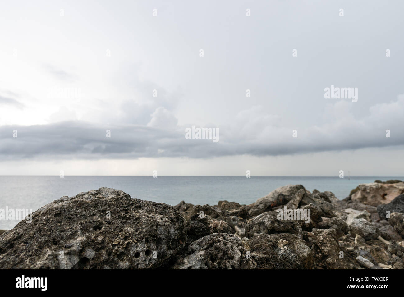 In the foreground in focus is a rocky shore. In the distance, the ocean and clouds Stock Photo