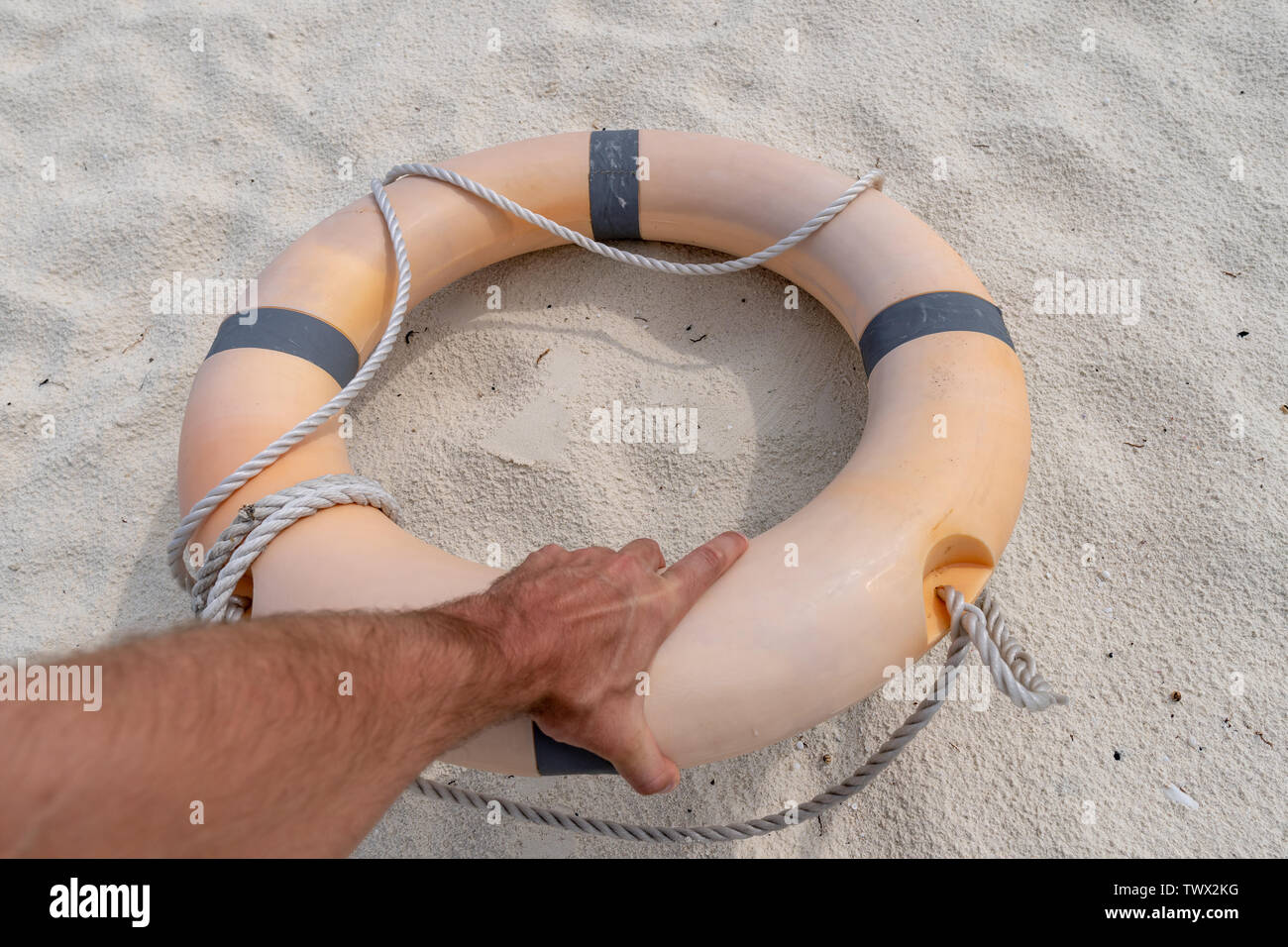 Male hand holding a life preserver. In the background sand Stock Photo