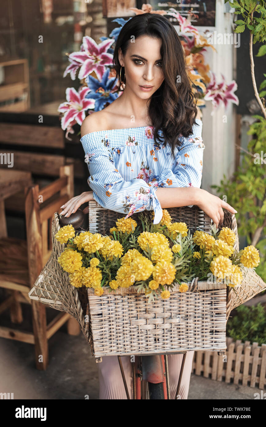 Brunette lady sitting on bike decorated with a bunch of flowers Stock Photo