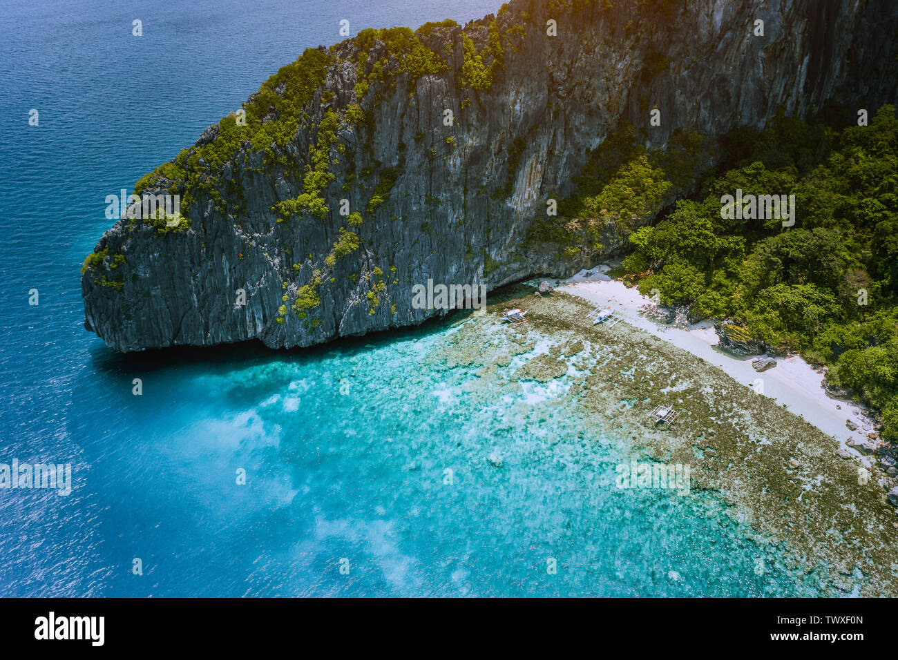 Aerial drone view of tropical beach with banca boats on Entalula Island. Karst limestone rocky mountains surrouns blue bay with beautiful coral reef Stock Photo