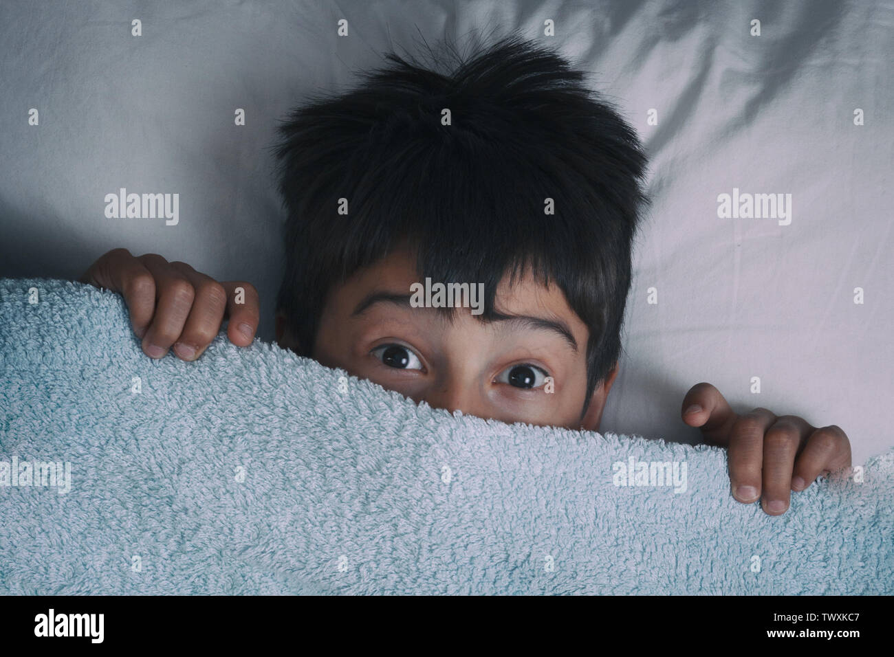 the boy lies on a bed the top view hid under a blanket for fear Stock