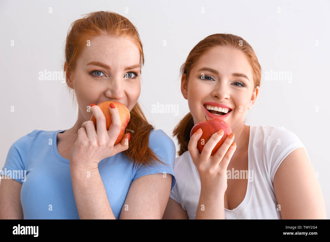 Beautiful young women eating fresh apples on light background Stock Photo