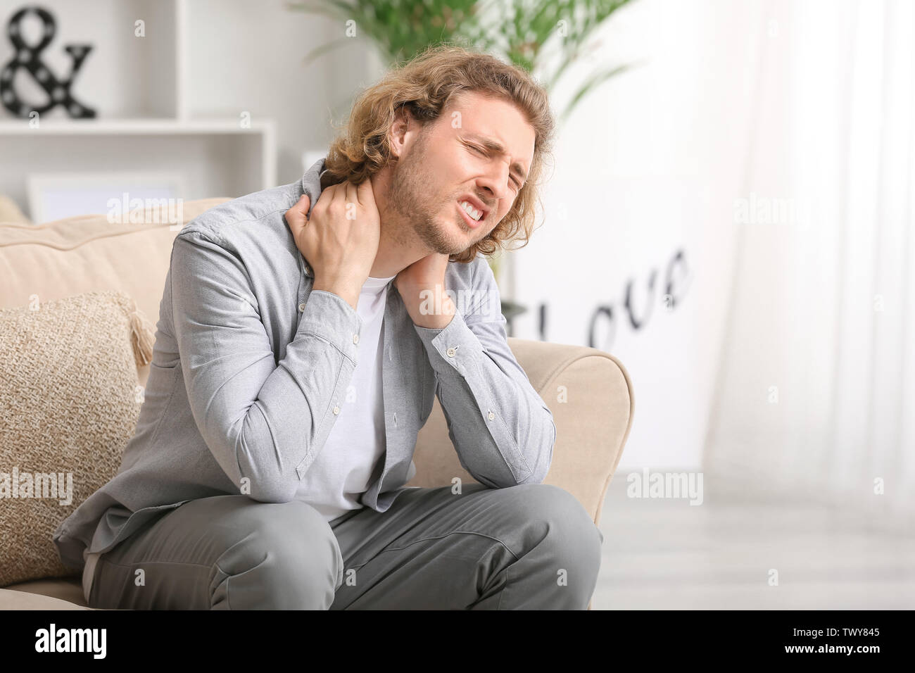 Young man suffering from neck pain at home Stock Photo - Alamy