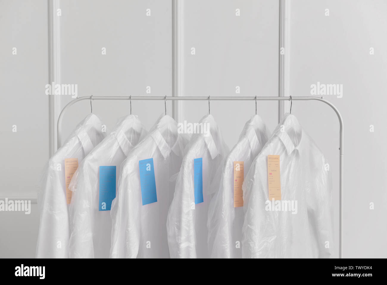 Rack with clothes after dry-cleaning near white wall Stock Photo - Alamy