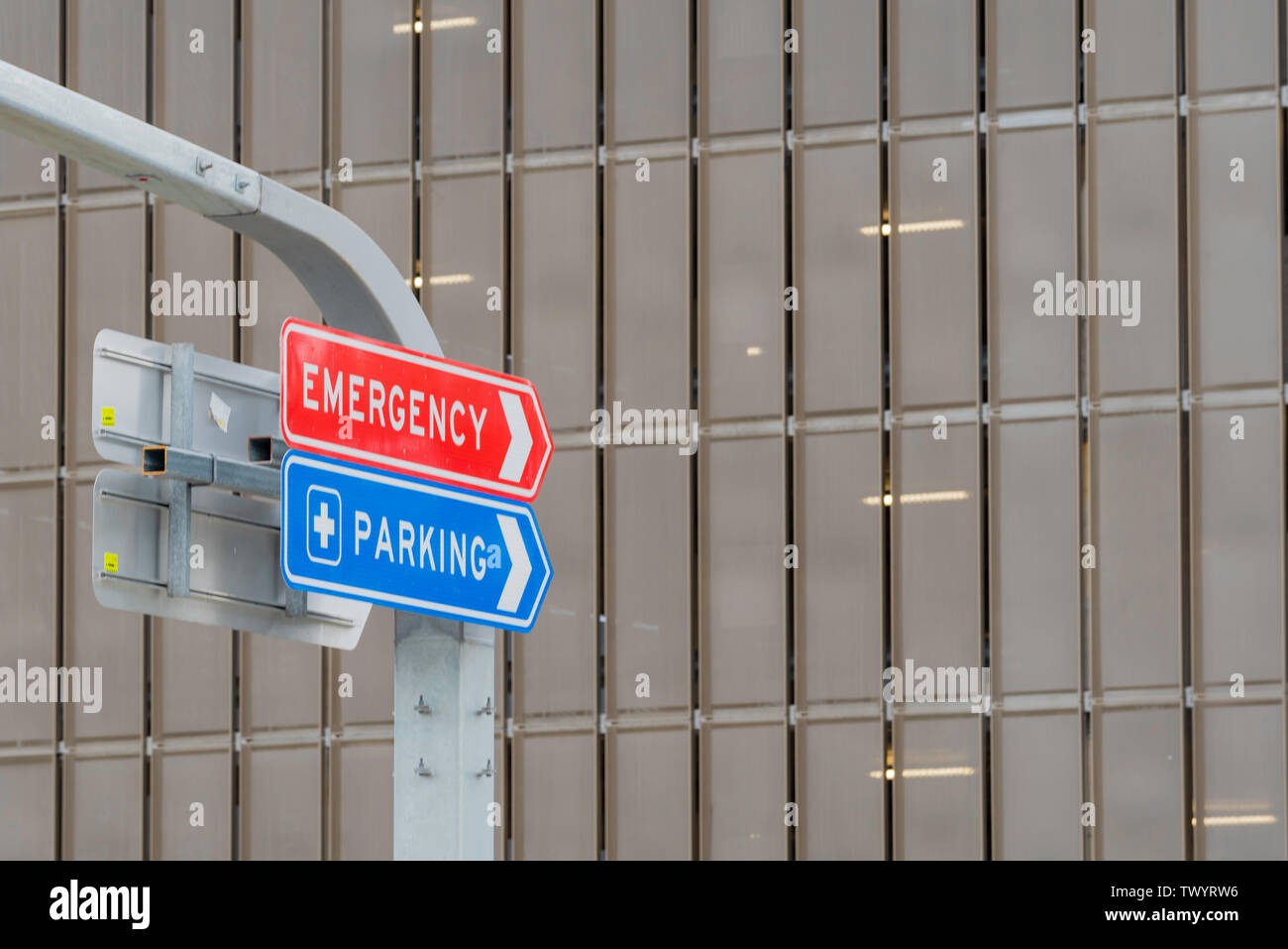 A red sign with white lettering saying Emergency and a blue sign with white lettering saying Parking at a hospital car park in Sydney, Australia Stock Photo