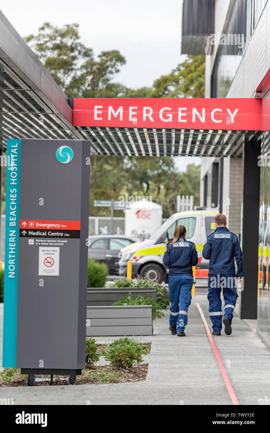 Two young white male and female paramedic ambulance officers walk towards an ambulance and Emergency sign at Sydney's new Northern Beaches Hospital Stock Photo
