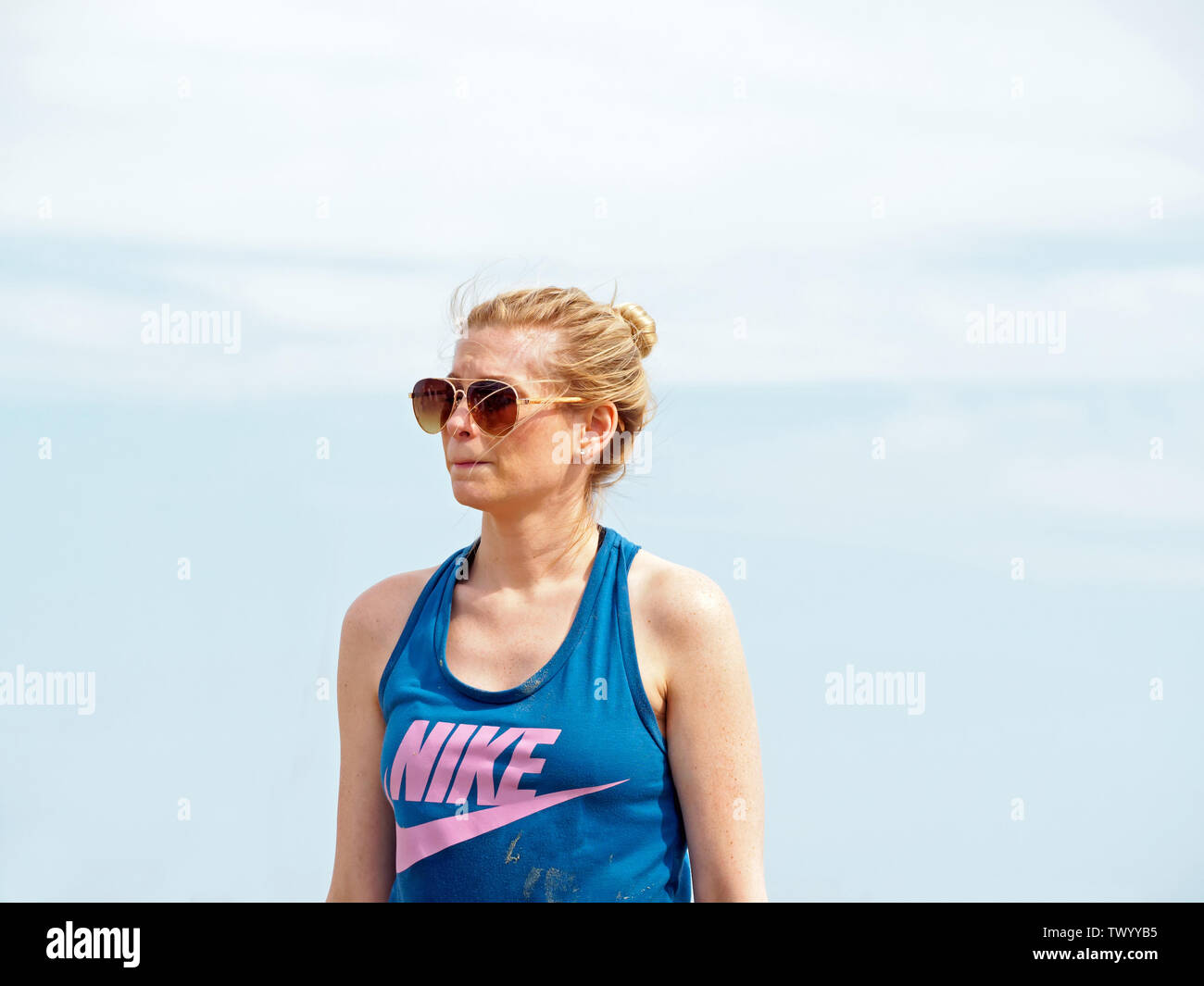 A thin blond woman in sunglasses and Nike tank top with the sky for background. Texas Sandfest 2019 in Port Aransas, Texas USA. Stock Photo