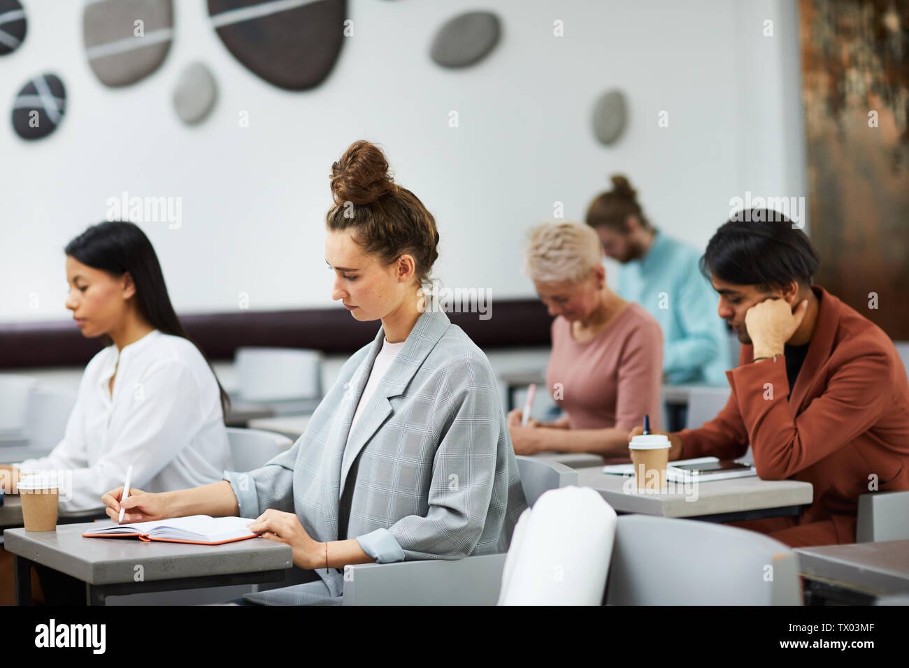 Side view of students writing notes in a row at the college lecture ...