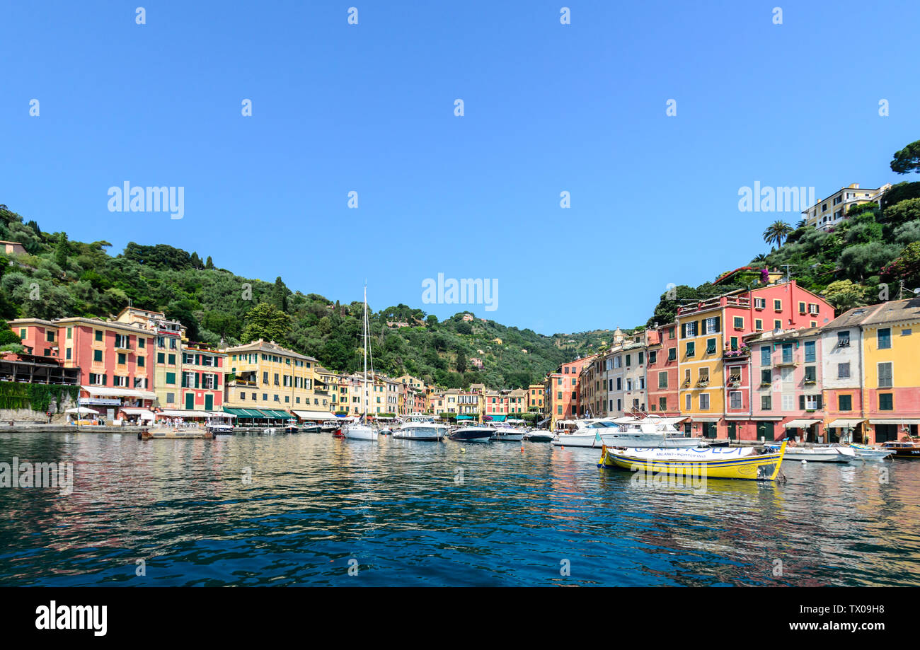 The boats and buildings of Portofino reflected in the harbour with the mountains and a clear blue sky in the background. Stock Photo