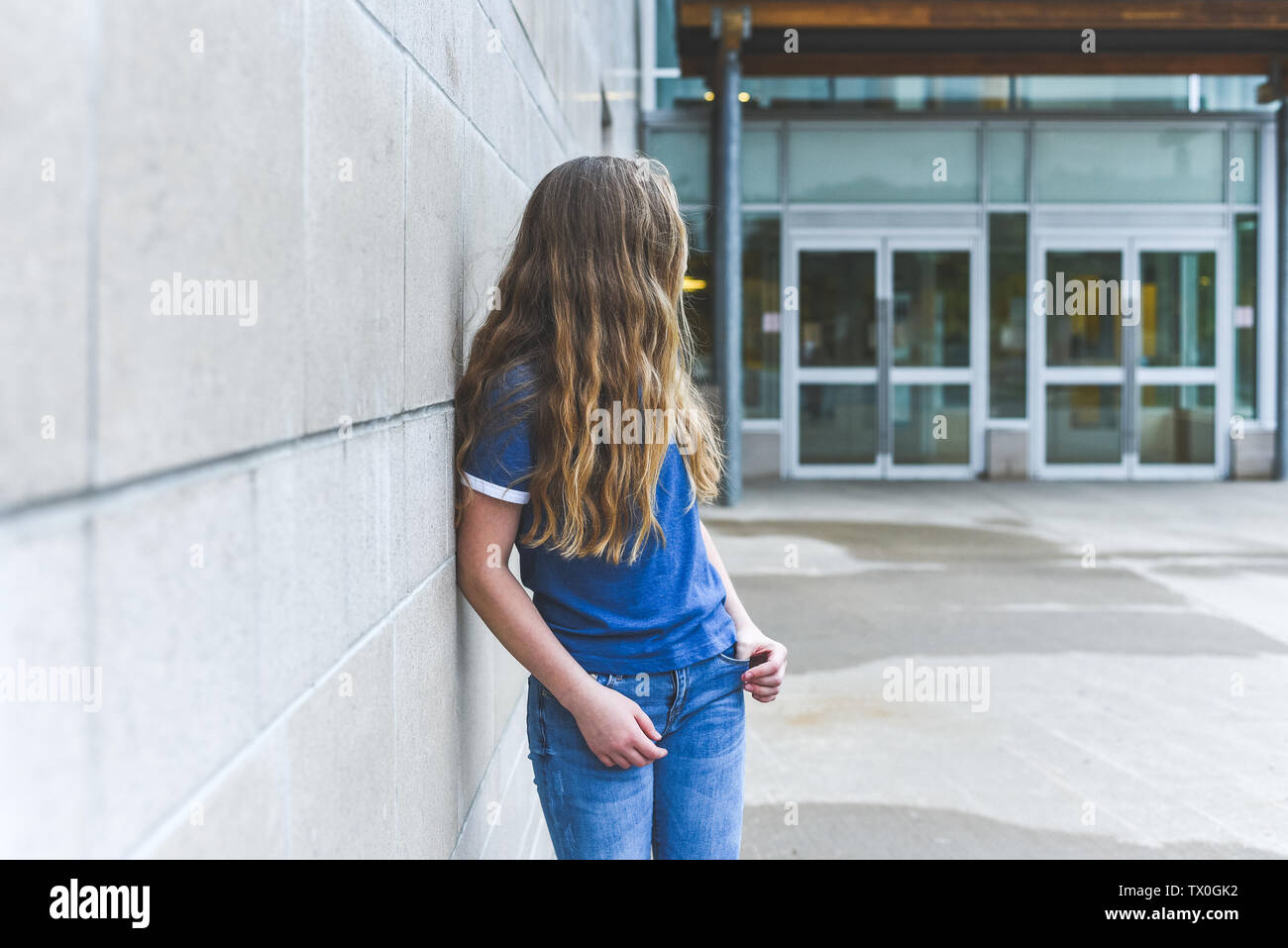 eenage girl looking over her shoulder while leaning against a brick wall. Stock Photo