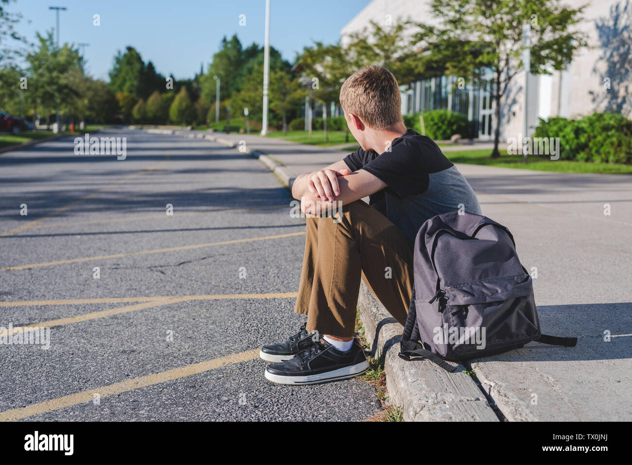 Lonely teenage boy sitting on curb next to high school Stock Photo - Alamy