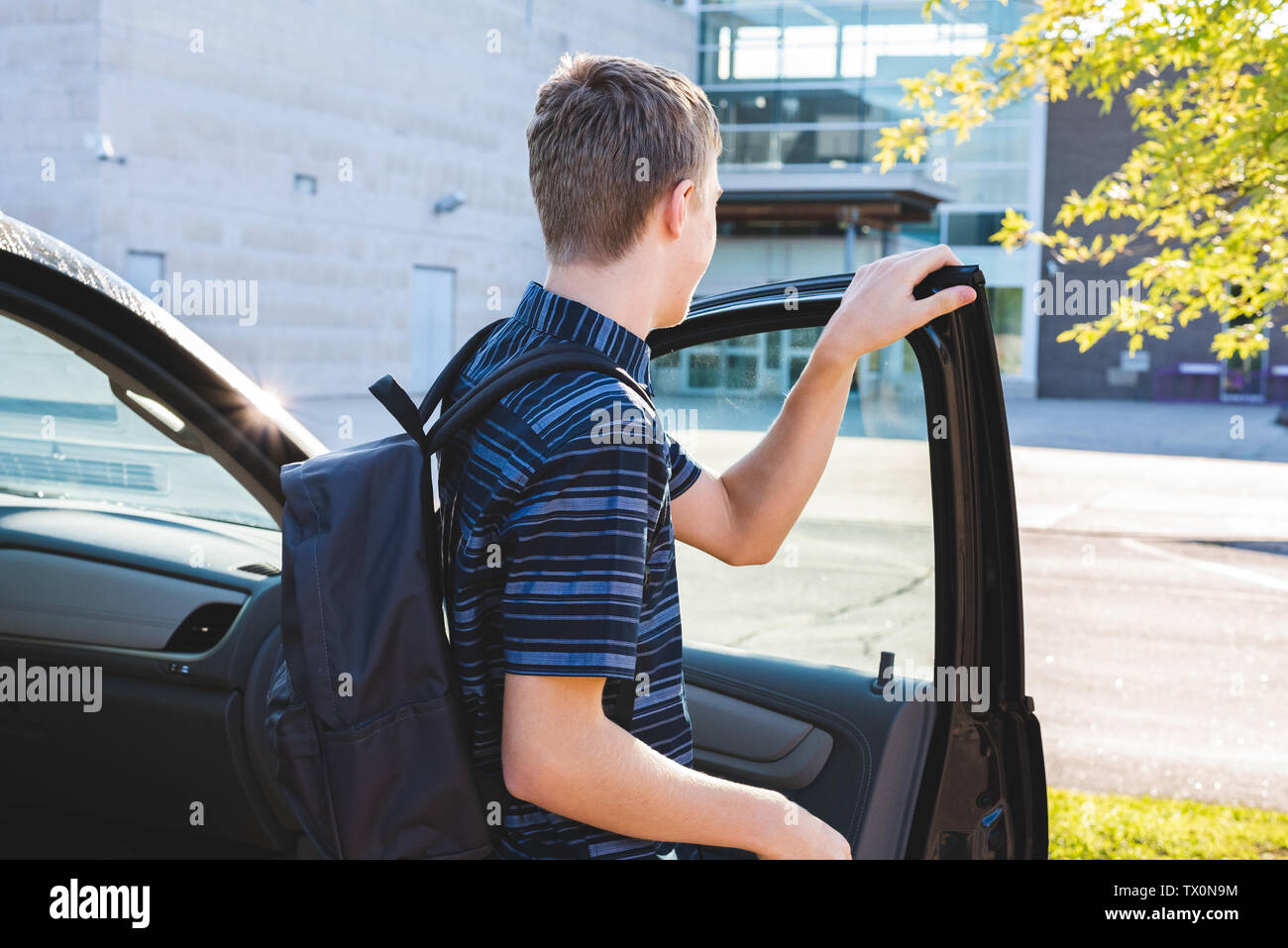 Teenager closing the door of his car that is parked in a school parking