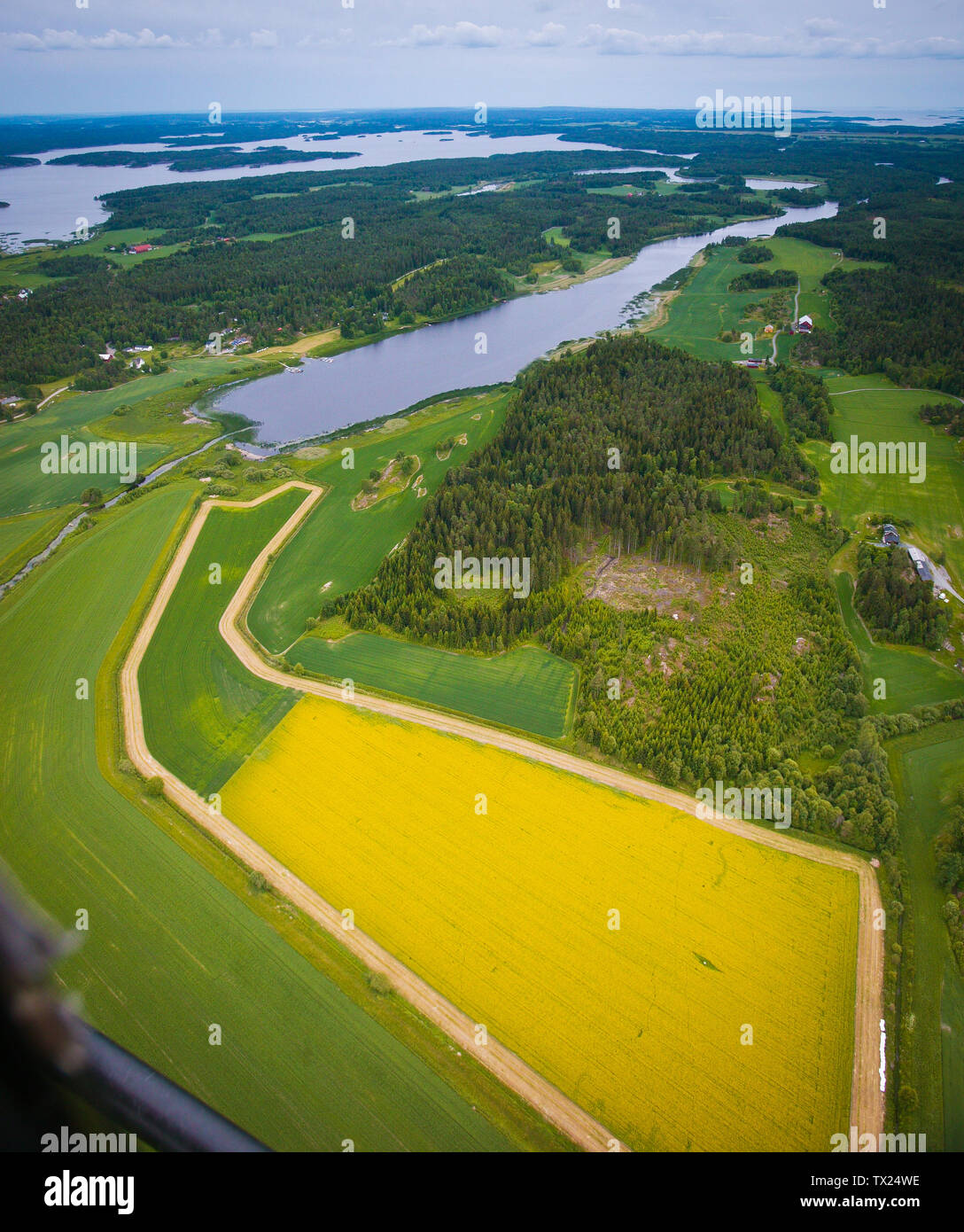 Aerial view over a part of the lake Vansjø and agricultural fields in Østfold, Norway, Scandinavia. Just above the center is the fjord Grepperødfjorden, and behind it is the open water area called Storefjorden. In the foreground is a field of mustard rapeseed. Vansjø is the largest lake in Østfold. The lake Vansjø and its surrounding lakes and rivers are a part of the water system called Morsavassdraget. The view is towards the southeast. June, 2006. Stock Photo