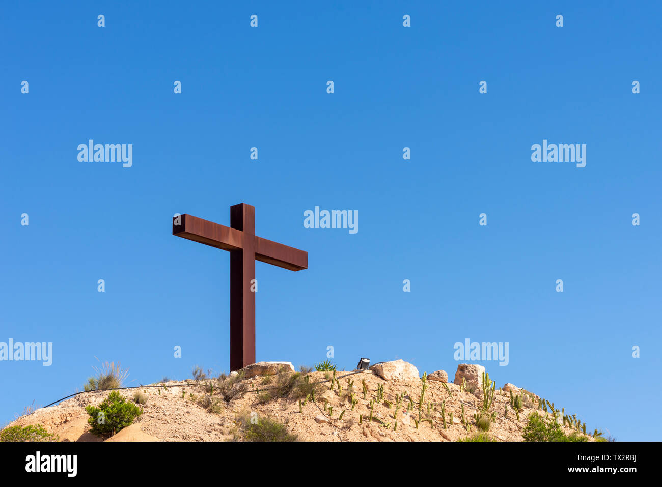 Rusty metal Christian religious cross on a hill above the town of Sucina, Murcia, Spain in blue sky. Space for copy Stock Photo