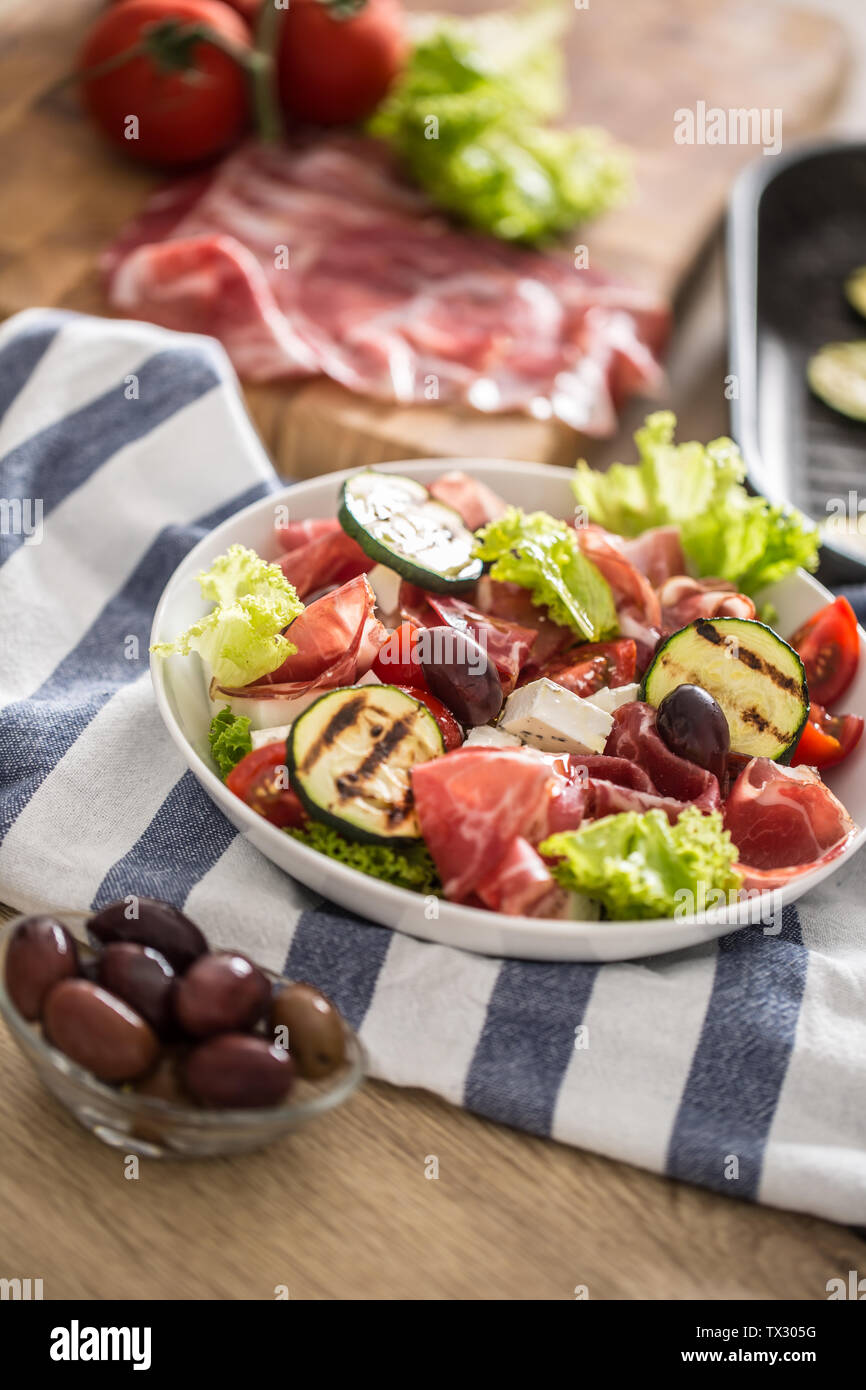 Fresh lettuce salad with grilled zucchini coppa di parma ham feta cheese olives tomatoes and olive oil Stock Photo