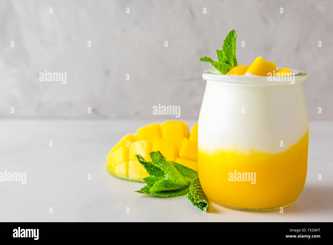 two glasses of <b>mango</b> <b>yogurt</b> with fresh fruits and mint over concrete backgr...