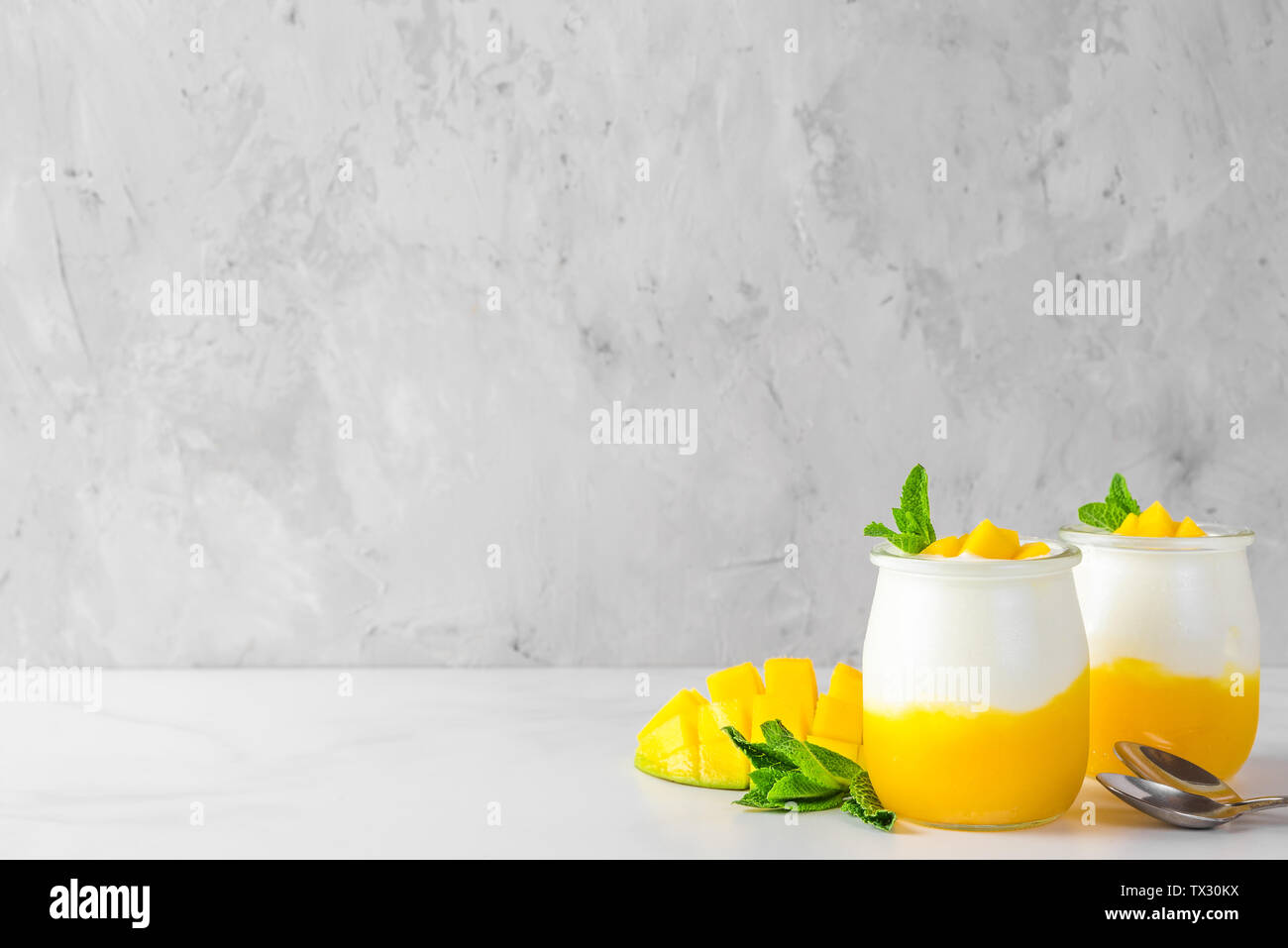 two glasses of mango yogurt with fresh fruits and mint over concrete background. healthy breakfast. close up Stock Photo