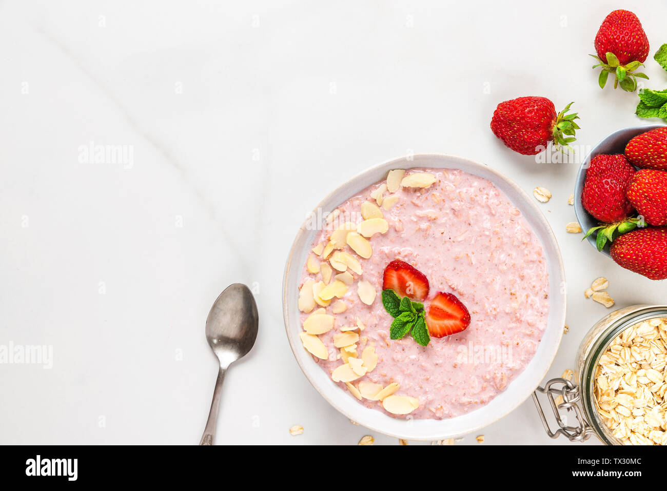 overnight strawberry oats with fresh berries, almonds and mint in a bowl with a spoon on white marble table. healthy breakfast. top view Stock Photo