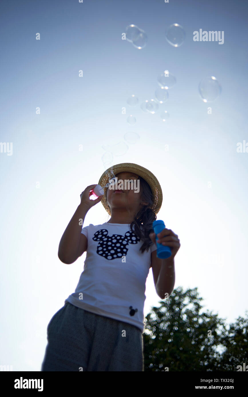 Stunning shots of a young Asian girl wearing a straw hat in summer sunshine blowing bubbles Stock Photo
