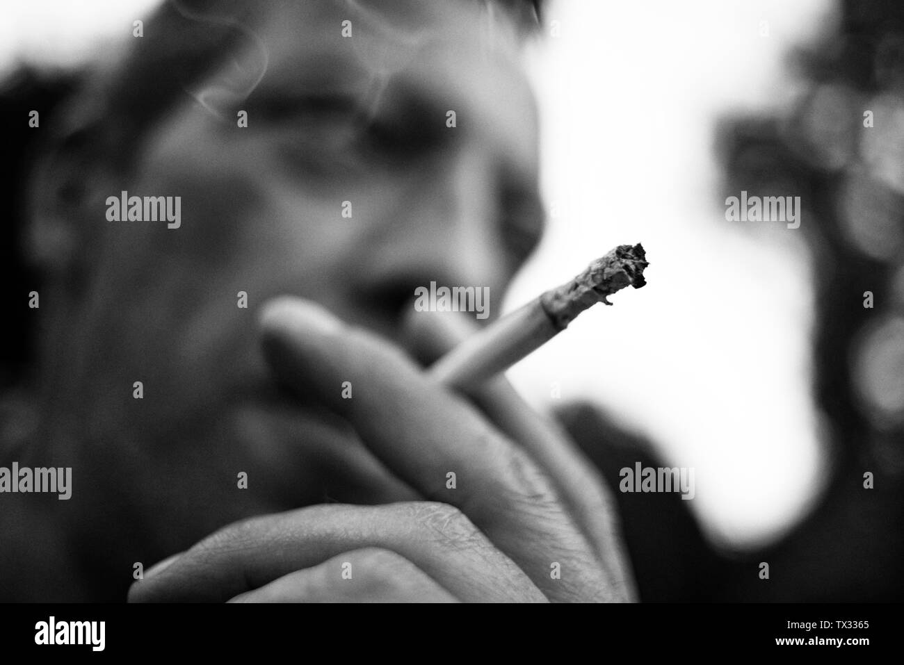 Stunning black and white close up of a man holding a cigarette in his hand and smoking it Stock Photo