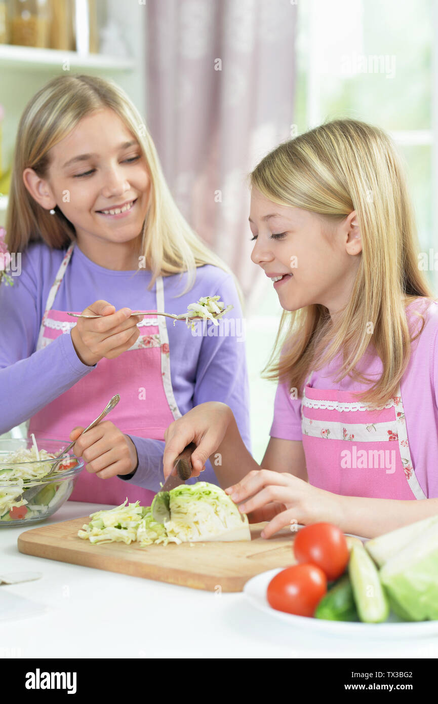 Two girls in pink aprons preparing salad Stock Photo