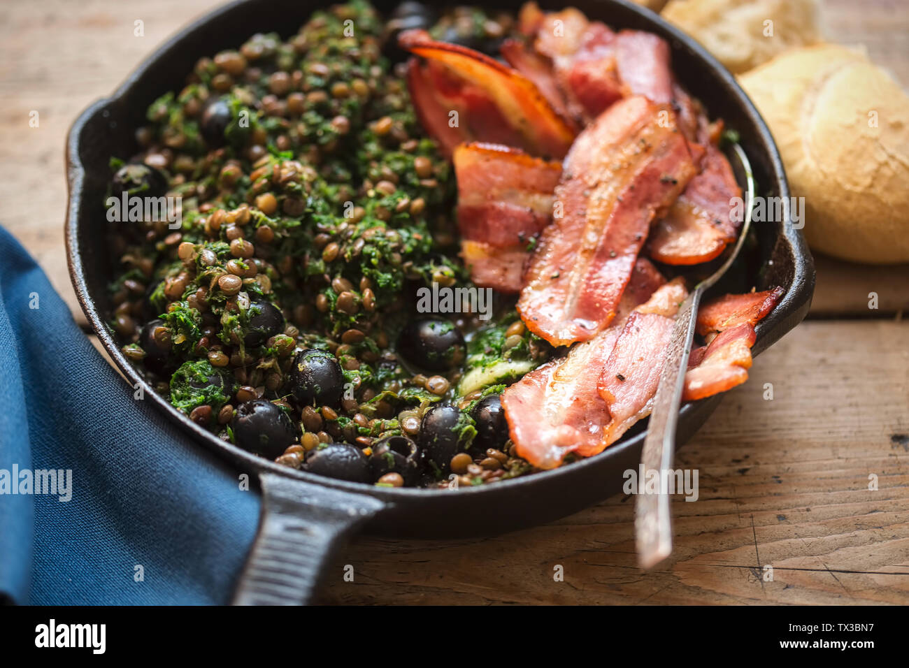 Brown lentils with spinach, black olives and fried bacon Stock Photo