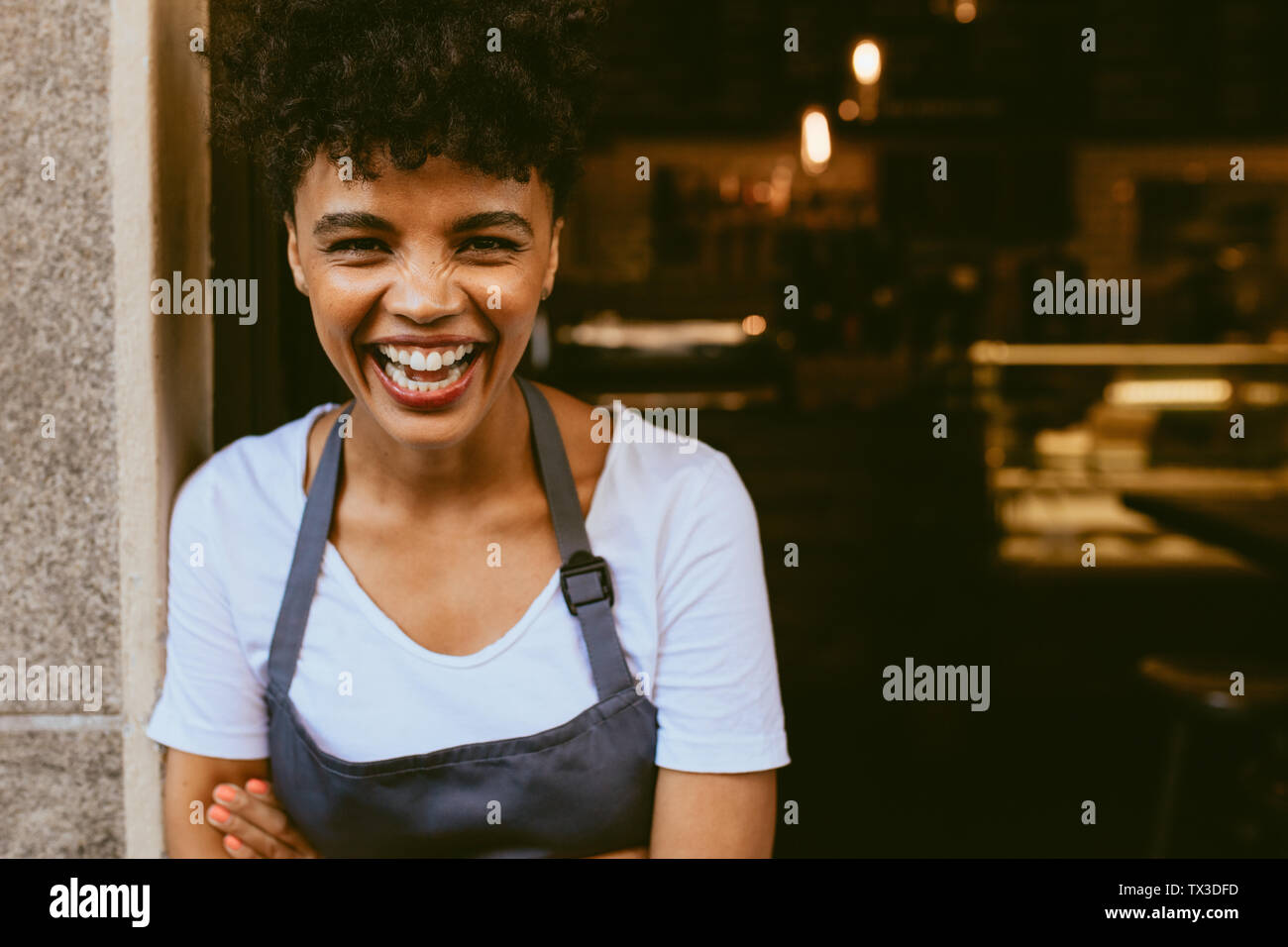 Cafe owner standing in the doorway of her coffee shop. Cheerful young