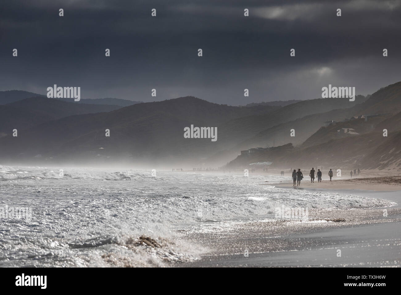 Ominous clouds over silhouetted people walking on ocean beach, Aireys Inlet, Victoria, Australia Stock Photo