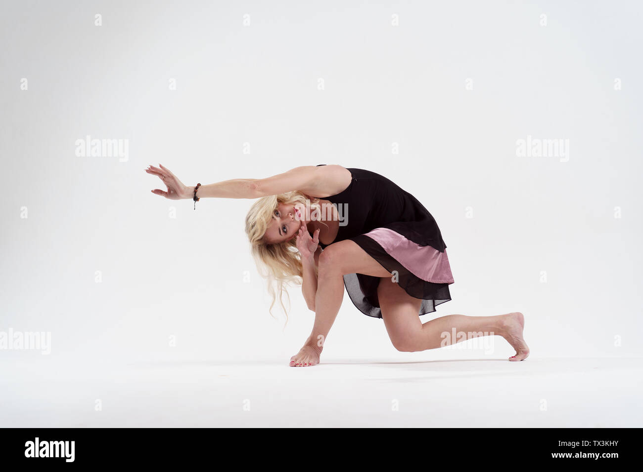 Photo of long-haired blonde looking to side with outstretched hand dancing in studio Stock Photo