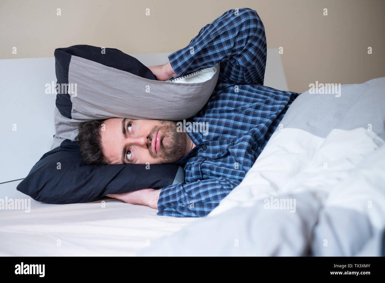 Man bothered by neighbor noise trying to sleep Stock Photo