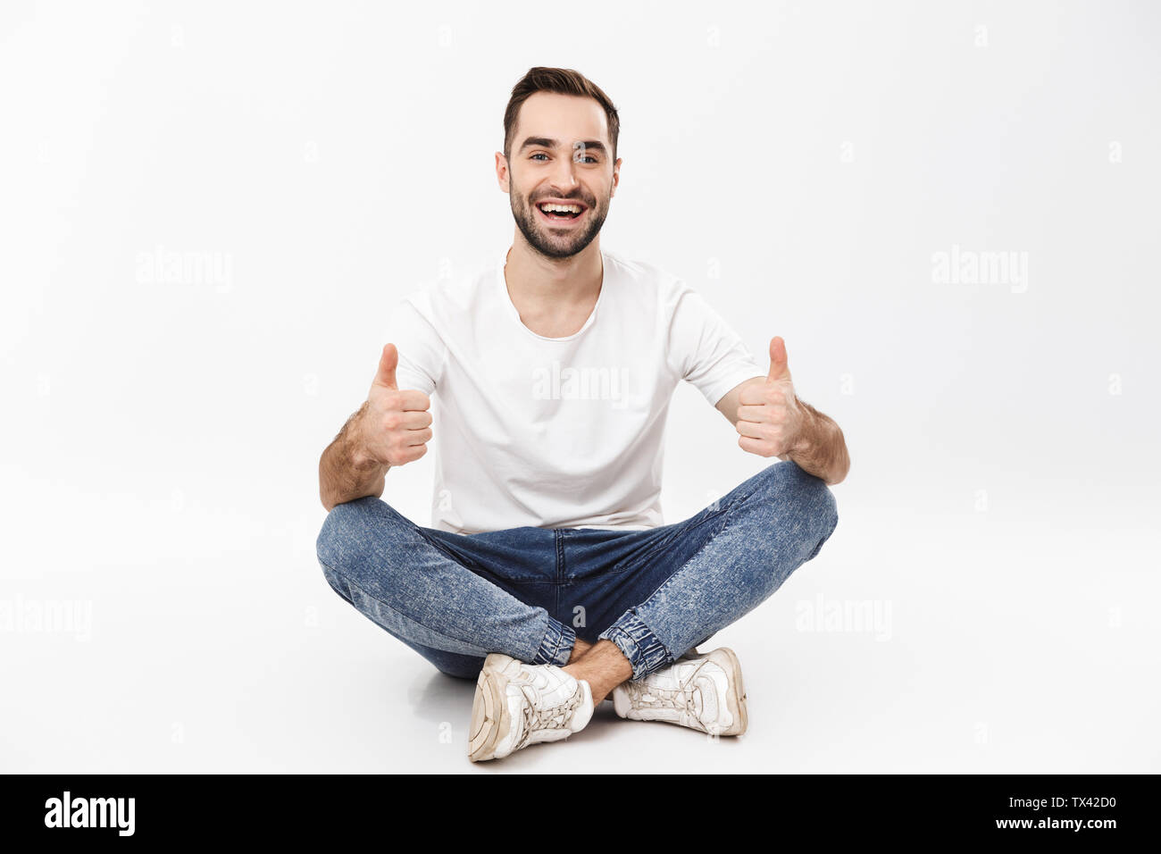 Full length of a cheerful young man sitting with legs crossed isolated ...