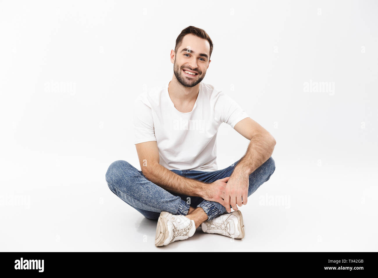 Full length of a cheerful young man sitting with legs crossed isolated ...