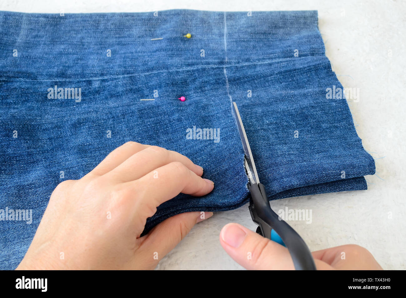 Woman hand holding a scissors and cutting blue denim shorts to make them shorter. Making jeans