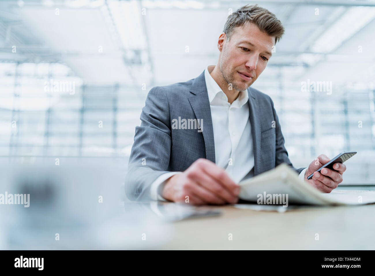 Businessman with cell phone reading newspaper in a cafe Stock Photo