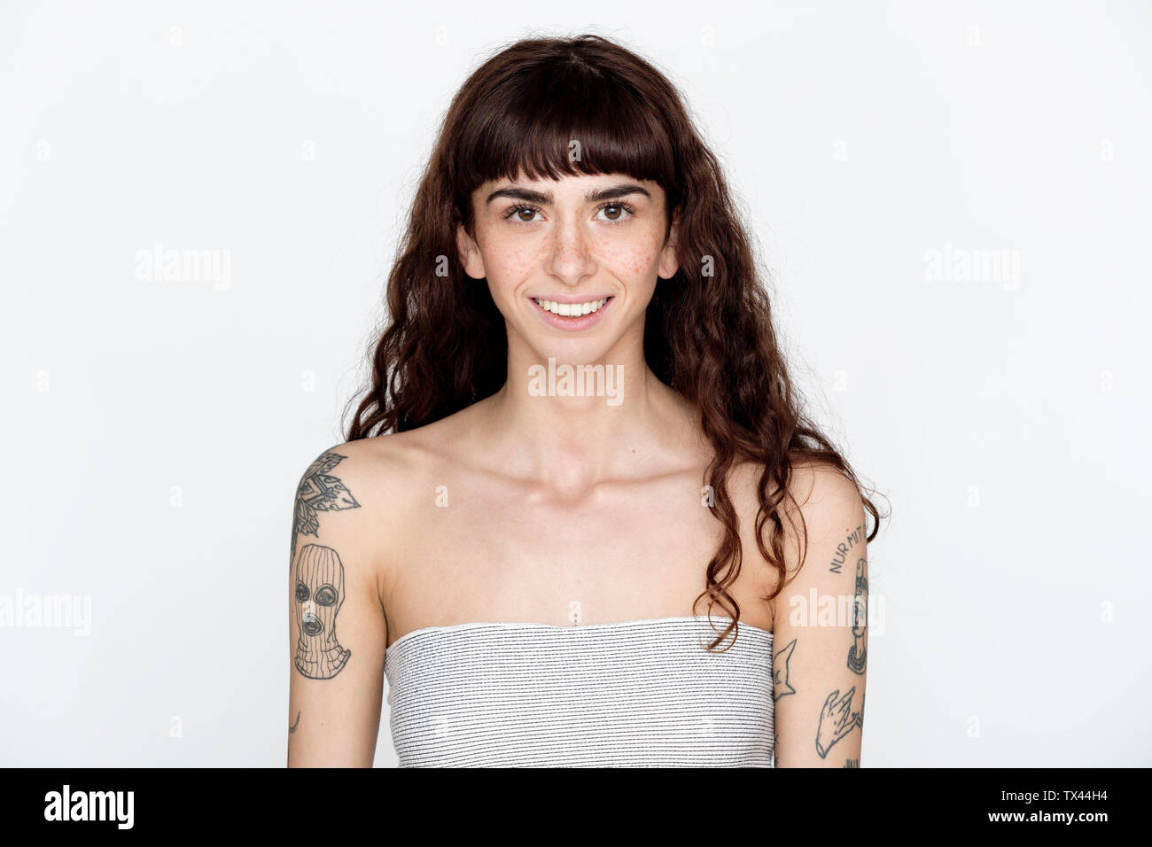 Portrait of smiling young woman with freckles and tattoos on her upper arms Stock Photo