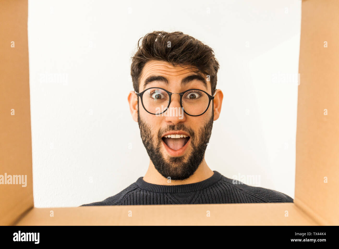 Portrait of surprised young man with beard and glasses looking into cardboard box Stock Photo