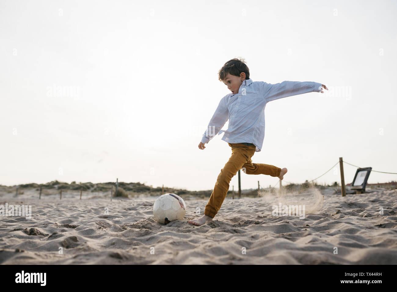Little boy playing soccer on the beach kicking the ball Stock Photo