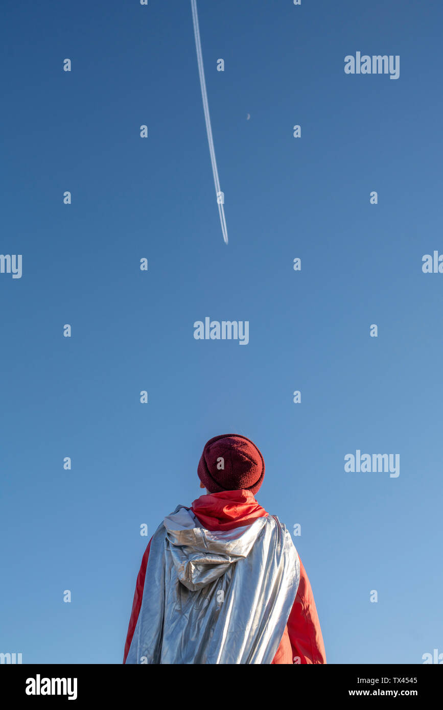 Rear view of boy dressed up as superhero looking at vapour trails in the sky Stock Photo